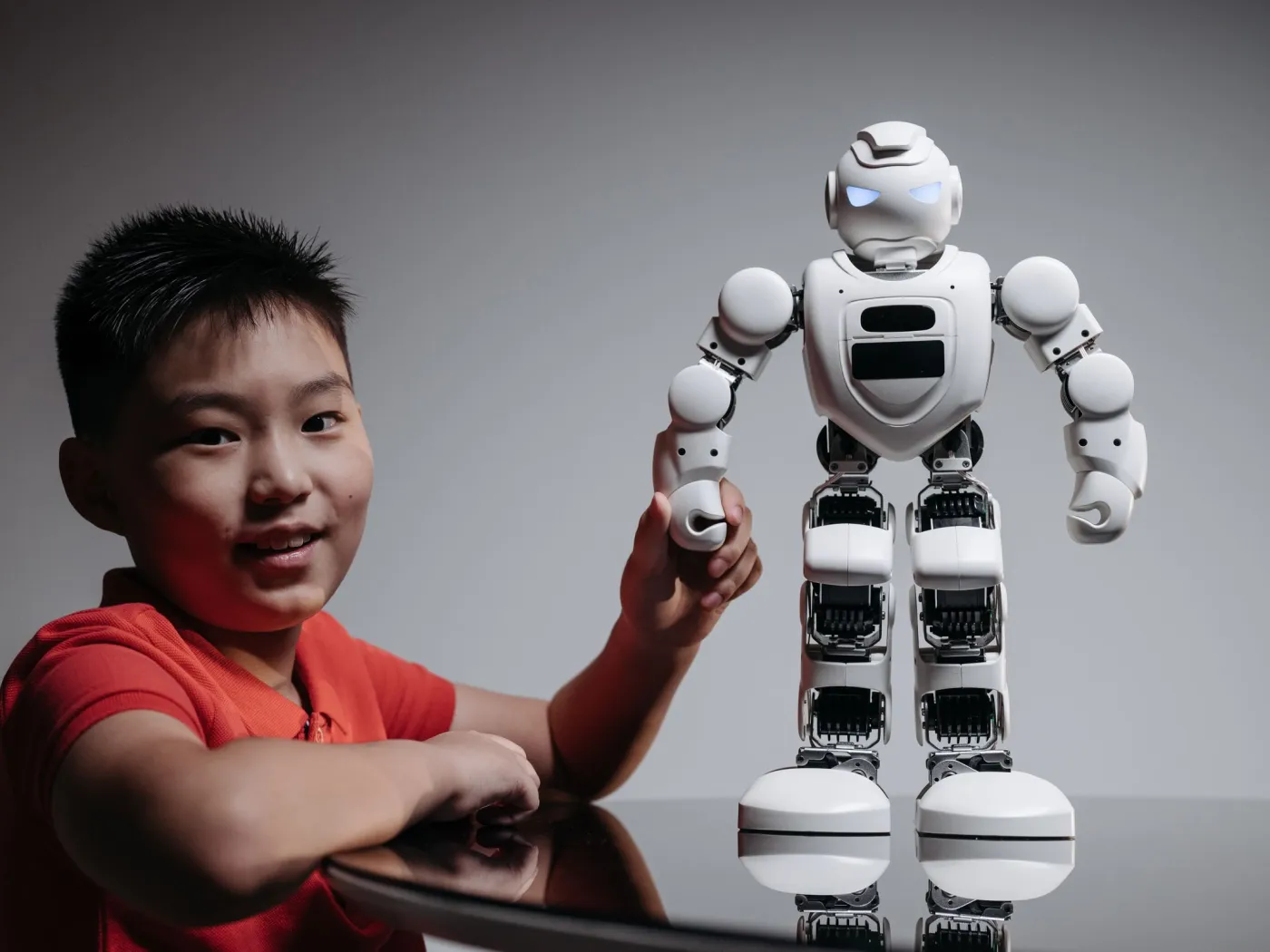 Smiling boy holding the hand of a white humanoid robot with glowing eyes