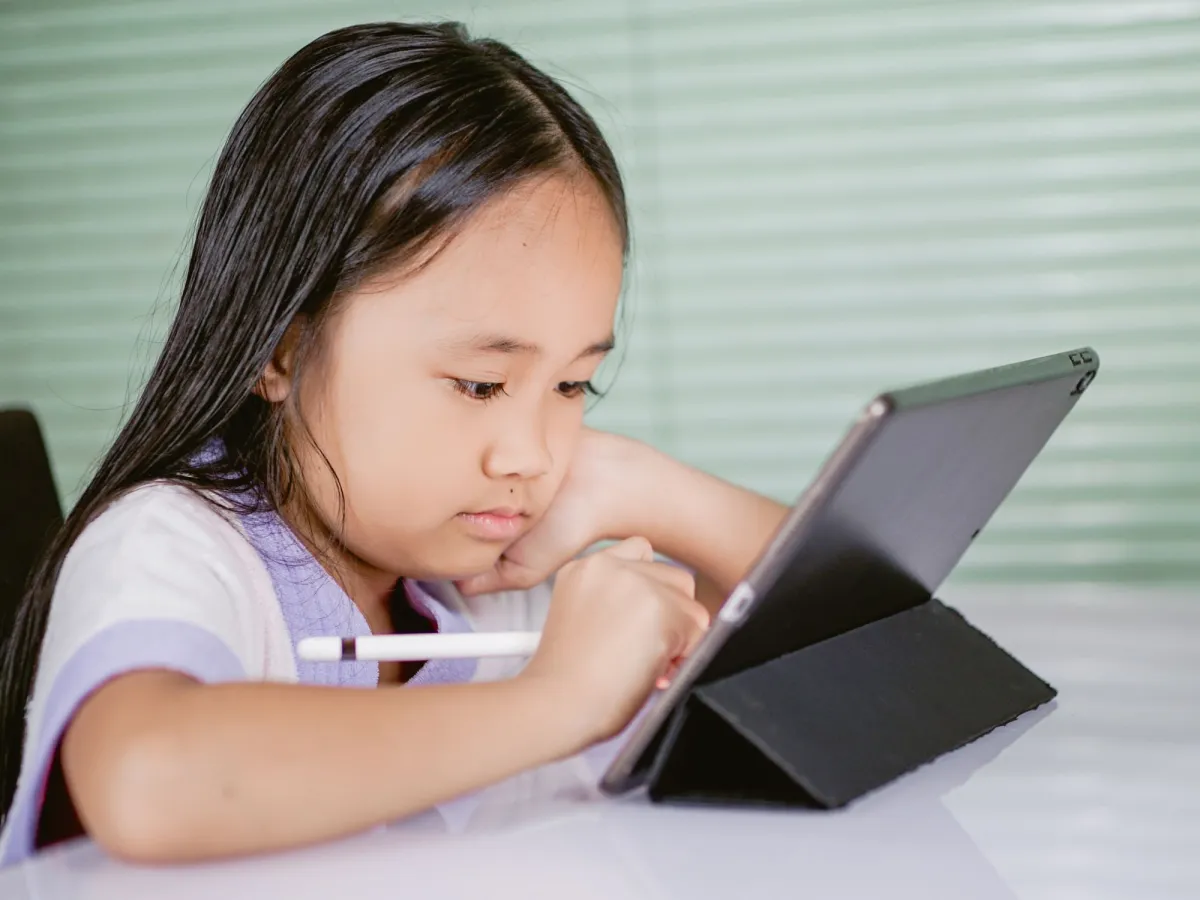 A young girl concentrates as she draws on a tablet with a digital stylus pencil.
