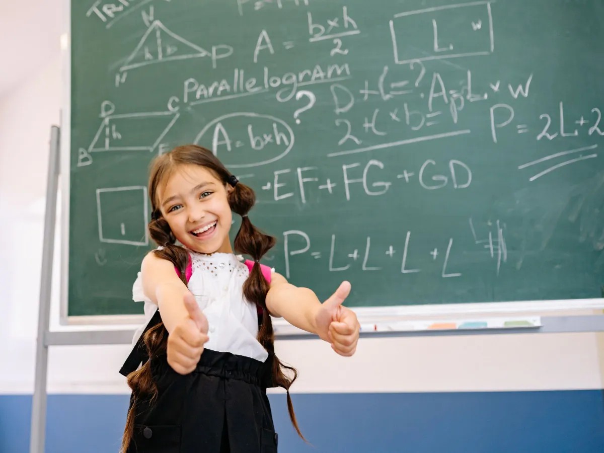 Beaming girl giving two thumbs up in front of a chalkboard full of geometry formulas