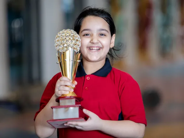 A beaming girl proudly holding up her trophy