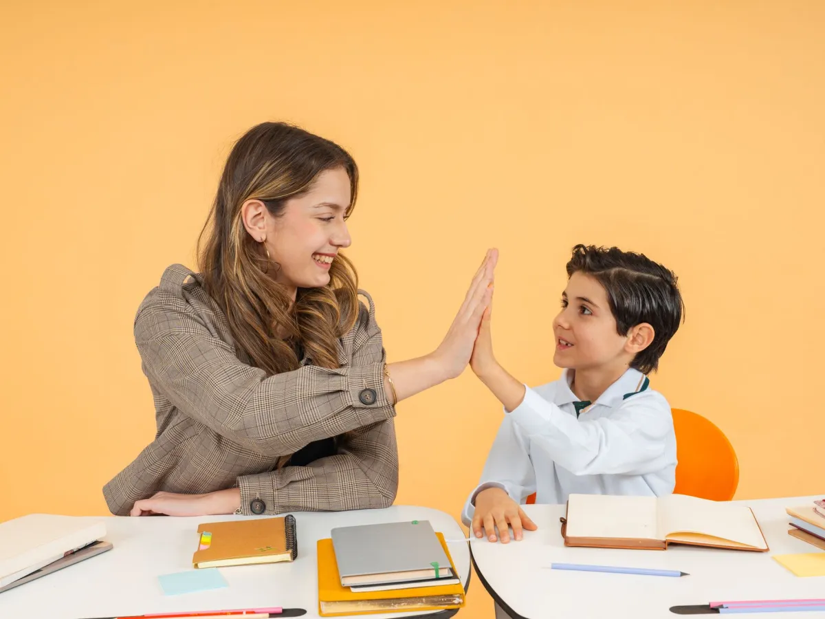 Friendly teacher high-fiving a young student at a desk